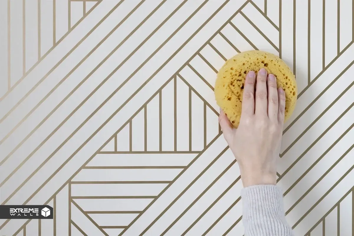 کاربردی ترین روش های ترمیم کاغذ دیواری پاره شده و آسیب دیده 12 اسفنج مرطوب در حال پاک کردن چسب اضافی اطراف کاغذ دیواری ترمیم شده